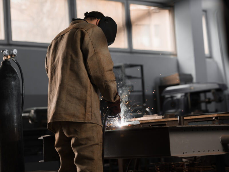 coded welder wearing protective gear, working on piece of steel
