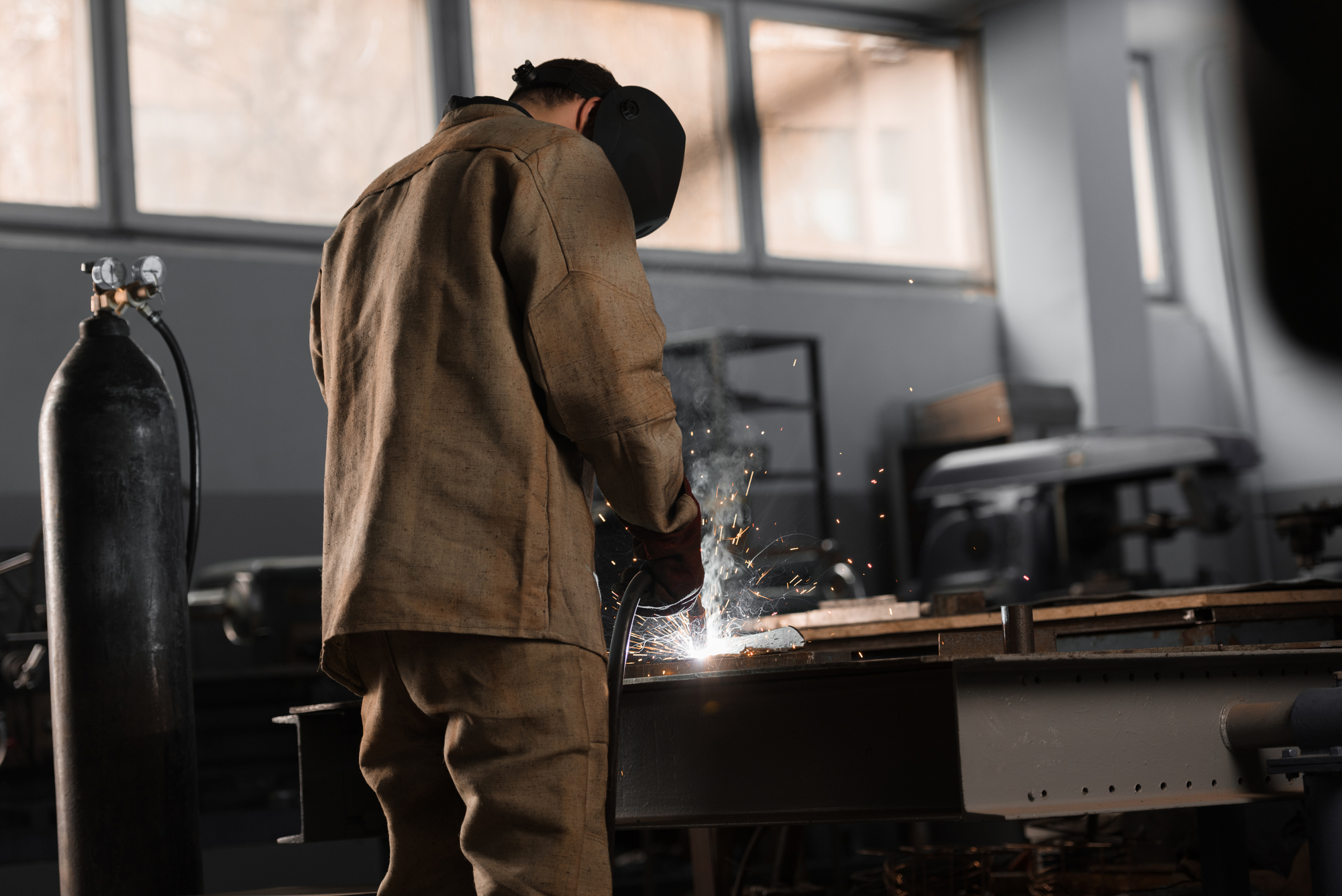 coded welder wearing protective gear, working on piece of steel
