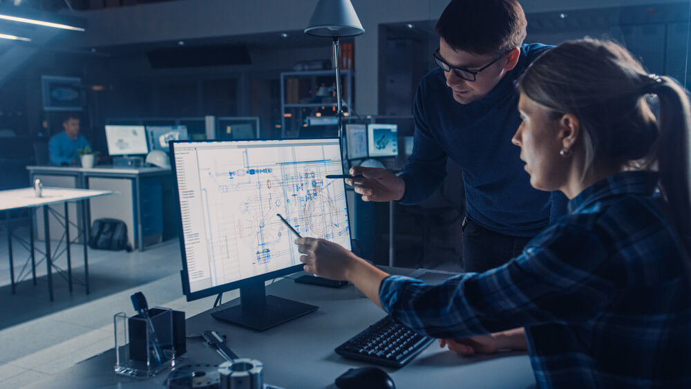 Man and woman pointing at a CAD drawing on a computer screen.